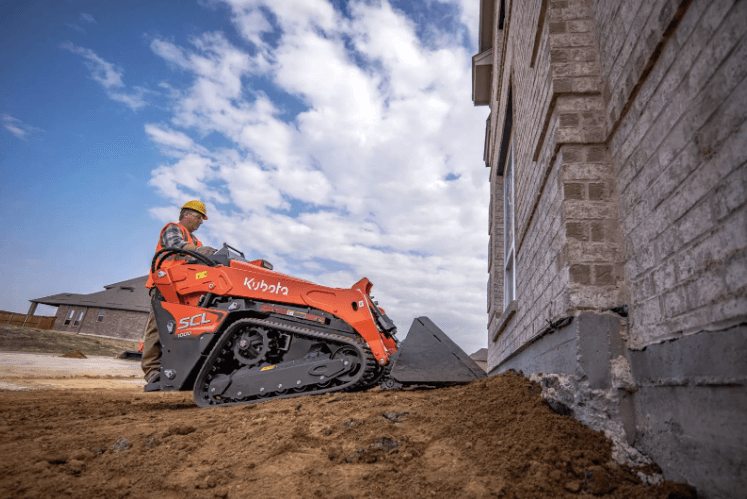 Man using a stand-on compact loader on construction site